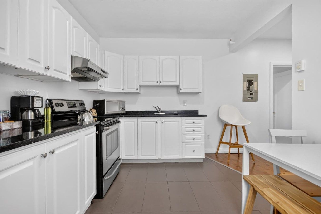 A modern kitchen with white cabinetry, a black countertop, and a wooden dining table.
