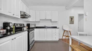 A modern kitchen with white cabinetry, a black countertop, and a wooden dining table.