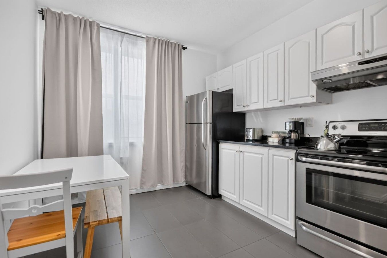 Een moderne keuken met witte kasten, roestvrijstalen apparatuur en een eethoek met een witte tafel en stoel.