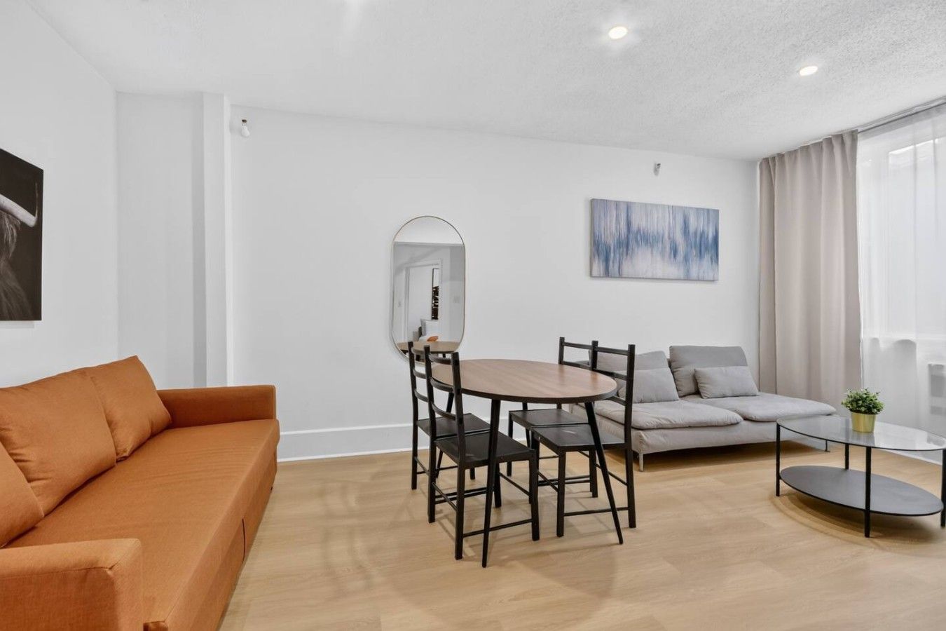 Un salon moderne comprenant un canapé, une table à manger avec des chaises, une table basse, un miroir et un tableau accroché au mur.