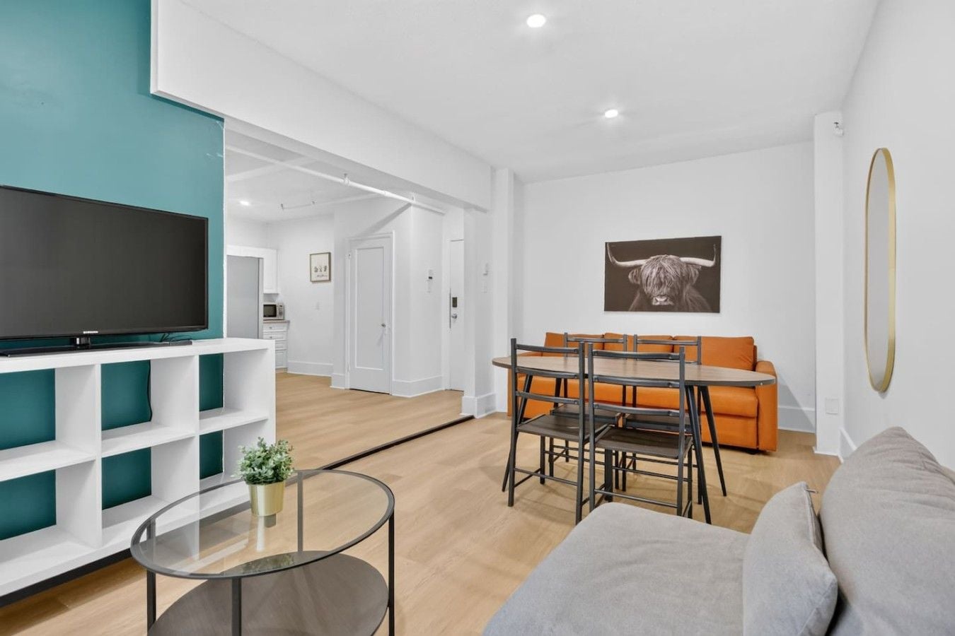Ein modernes Wohnzimmer mit einem Flachbildfernseher, einem Glastisch, einem Essbereich mit Tisch und Stühlen sowie einem Sofa.