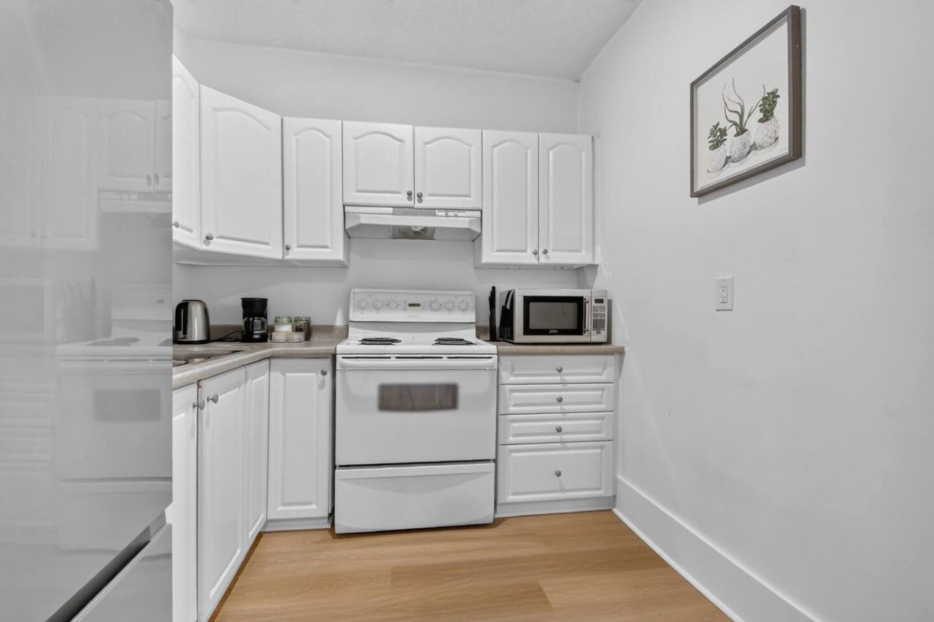 Une cuisine avec des meubles blancs, une cuisinière, un four à micro-ondes et un petit tableau encadré accroché au mur.