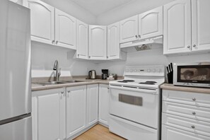 A kitchen with white cabinets, a stainless steel sink, a stove, and a microwave. - Modern 1BR Oasis | Steps to City Highlights (Gatineau)