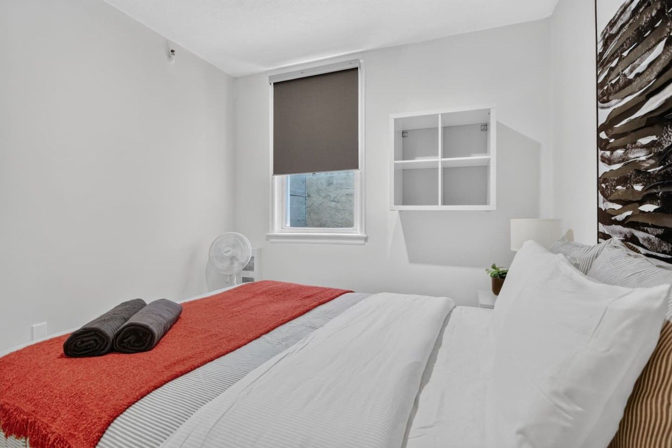 Une chambre d’hôtel moderne équipée d’un lit, d’une fenêtre, d’une table de chevet et d’une étagère fixée au mur.