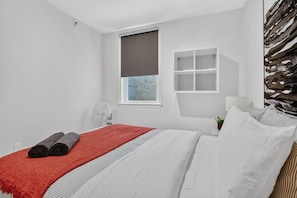 Habitació d'hotel moderna amb un llit, una finestra, una taula de nit i una estantanya penjada a la paret.