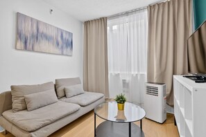 Een moderne woonkamer met een bank, een glazen salontafel en een witte airconditioning.