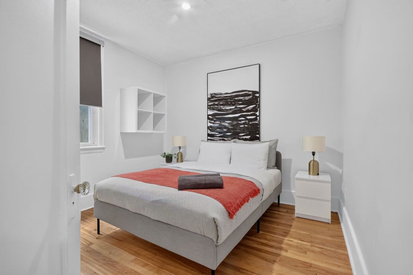 Ein modernes Schlafzimmer mit einem Bett, Nachttischen, einem Fenster und einem an der Wand befestigten Kunstwerk.