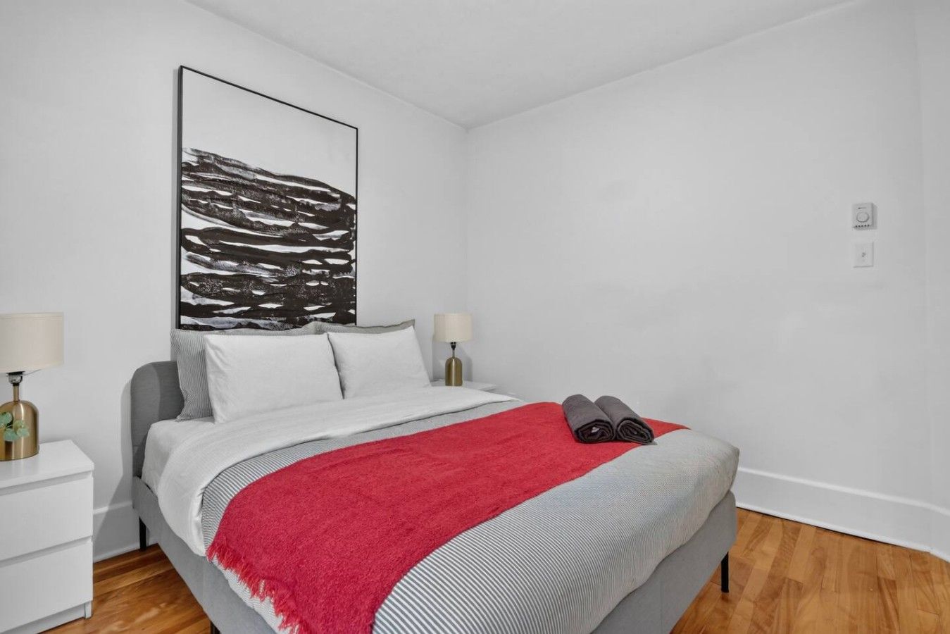 A modern bedroom with a bed, two bedside tables, a red throw blanket, and a large abstract painting on the wall.