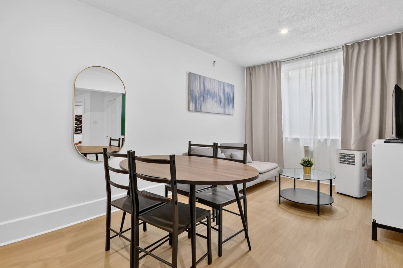 Un salon moderne avec une table à manger ronde, des chaises, un canapé, un téléviseur et une grande fenêtre avec des rideaux.