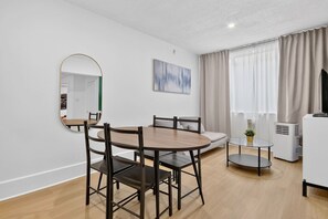 Een moderne woonkamer met een ronde eettafel, stoelen, een bank, een televisie en een groot raam met gordijnen.