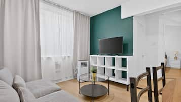 Una sala de estar moderna con un sofá, una mesa de centro de vidrio, un televisor sobre un estante blanco y una pequeña planta.