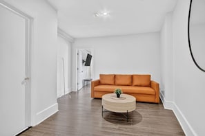 Un couloir avec un canapé et une table basse ronde, une porte et un luminaire au plafond.