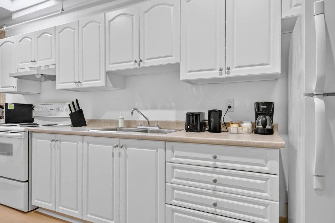 Una cocina con armarios blancos, estufa, pileta y cafetera.