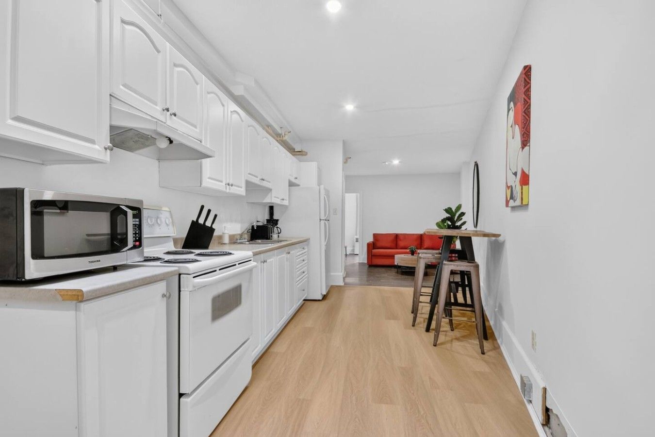 A modern kitchen with white cabinetry, a microwave, stove, and a dining area with stools.