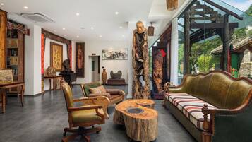 Un vaste espace de vie agrémenté d’un canapé vert, de chaises en bois, d’une table basse ronde en bois et d’une grande sculpture en bois.