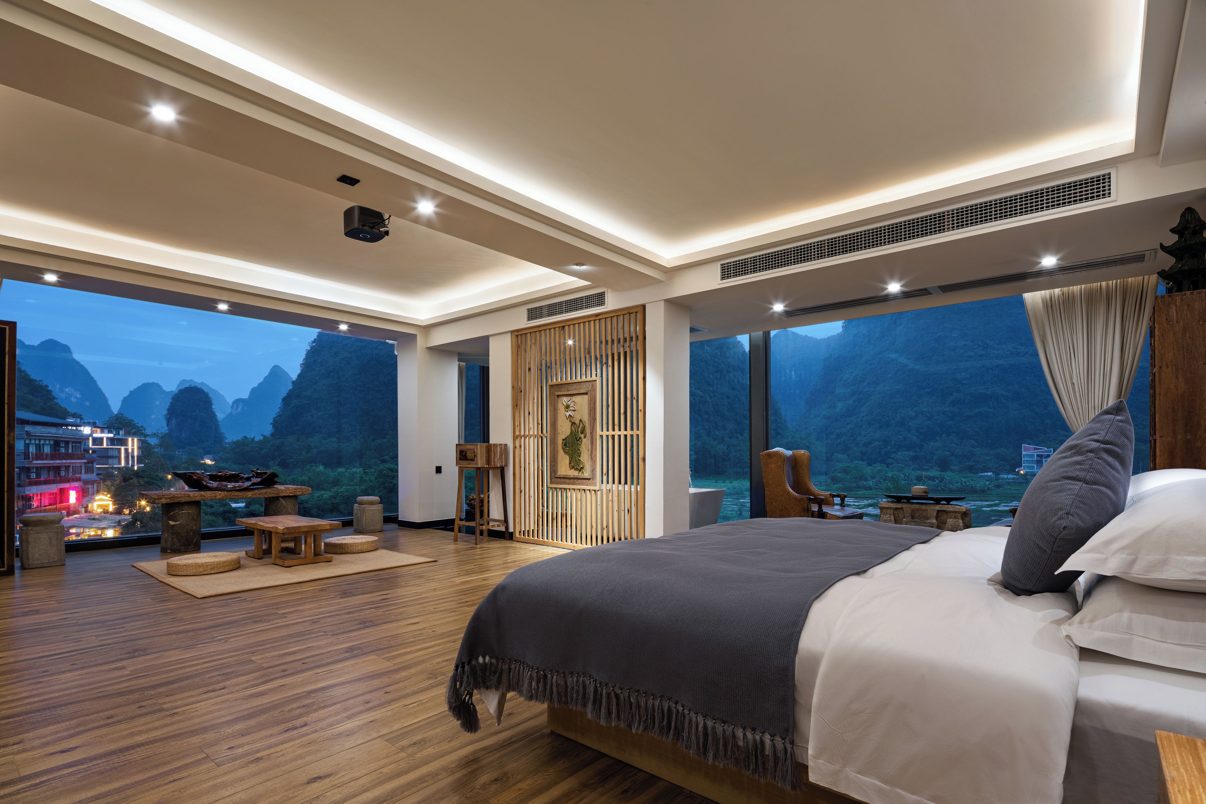 Une chambre spacieuse avec un grand lit, un plancher en bois, une vue sur les montagnes et un balcon équipé d’une table et de chaises.