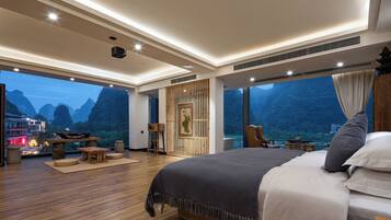 Une chambre spacieuse avec un grand lit, un plancher en bois, une vue sur les montagnes et un balcon équipé d’une table et de chaises.