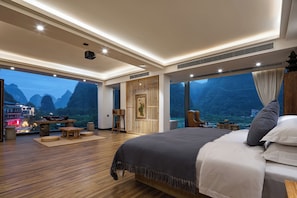 Un dormitorio espacioso con una cama grande, piso de madera, vista a las montañas y un balcón con mesa y sillas.