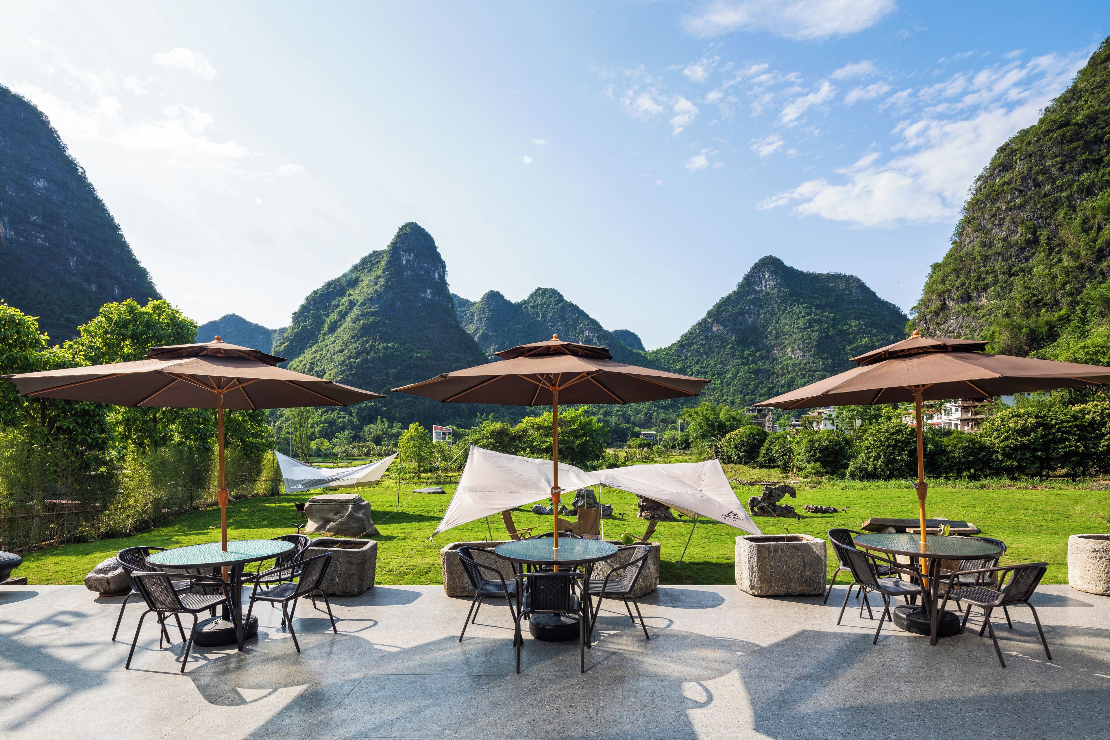 An outdoor seating area with tables and chairs, umbrellas, and a view of mountainous terrain.