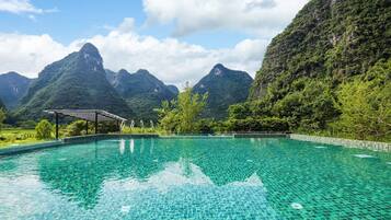 Una piscina cristalina con borde de azulejos, rodeada de exuberante vegetación y montañas al fondo.