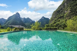 A clear pool with a tiled edge, surrounded by lush greenery and mountains in the background. - Chennianwangshiyisu (Guilin)