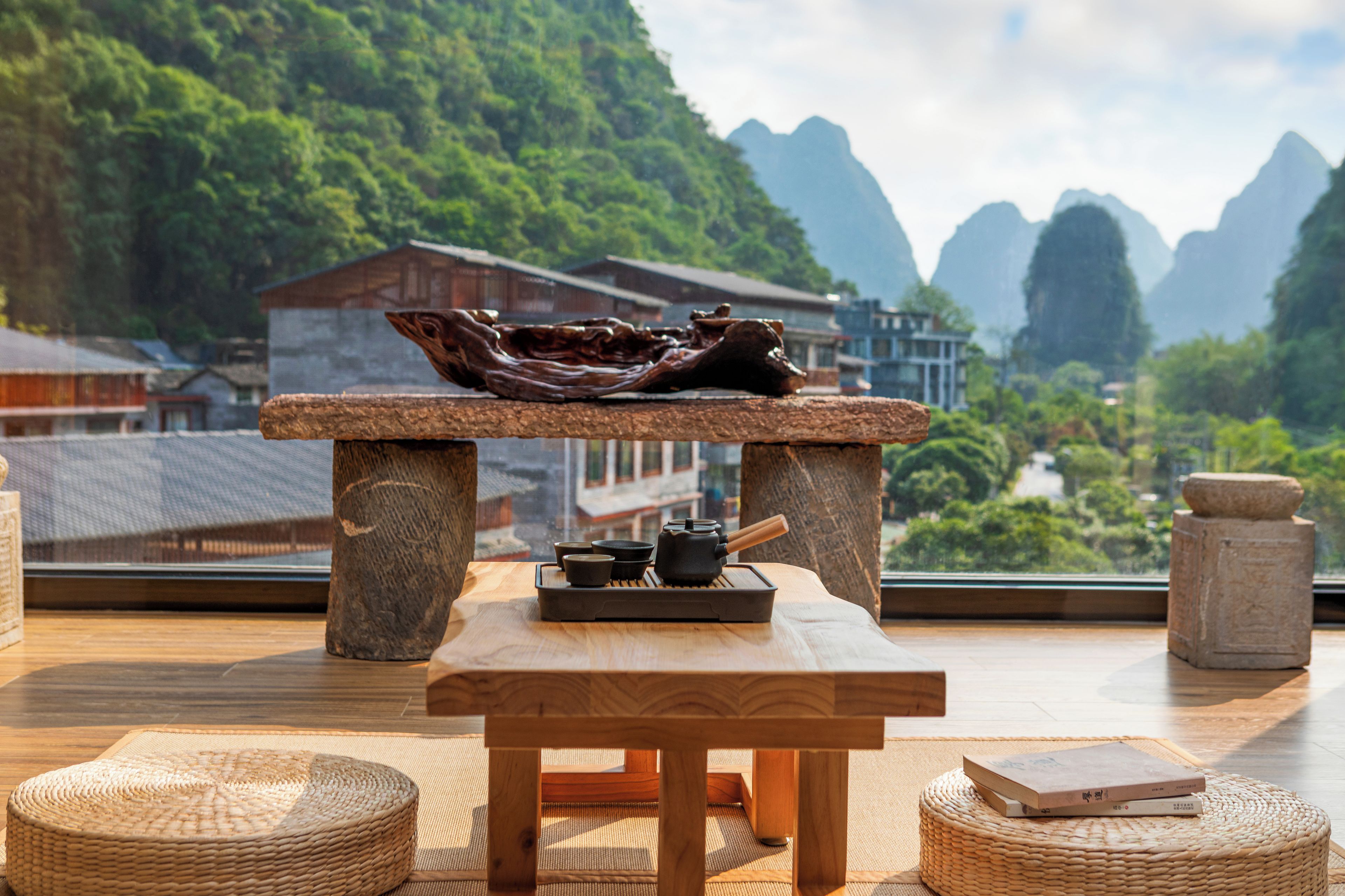 A wooden table with a traditional dish and tea set, set against a backdrop of a mountainous landscape and traditional architecture.