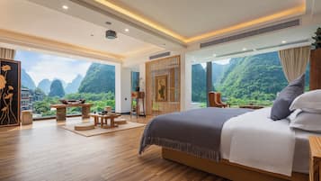 A spacious bedroom with a large bed, a wooden floor, and a view of lush greenery.