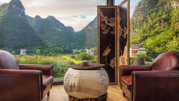 Une pièce comprenant deux fauteuils en cuir, une table en bois ornée d’un vase décoratif, et offrant une vue sur un paysage montagneux.