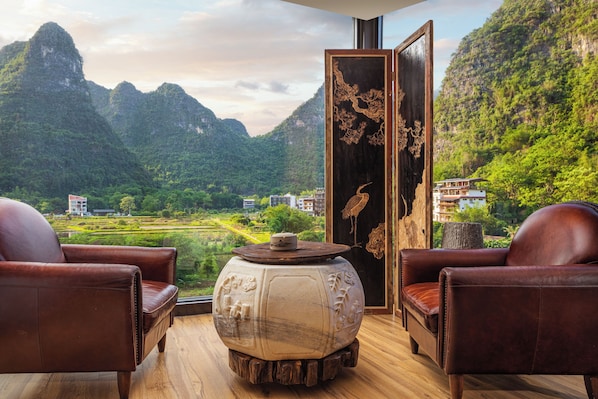 Una habitación con dos sillones de cuero, una mesa de madera con un jarrón decorativo, y vistas a un paisaje montañoso.