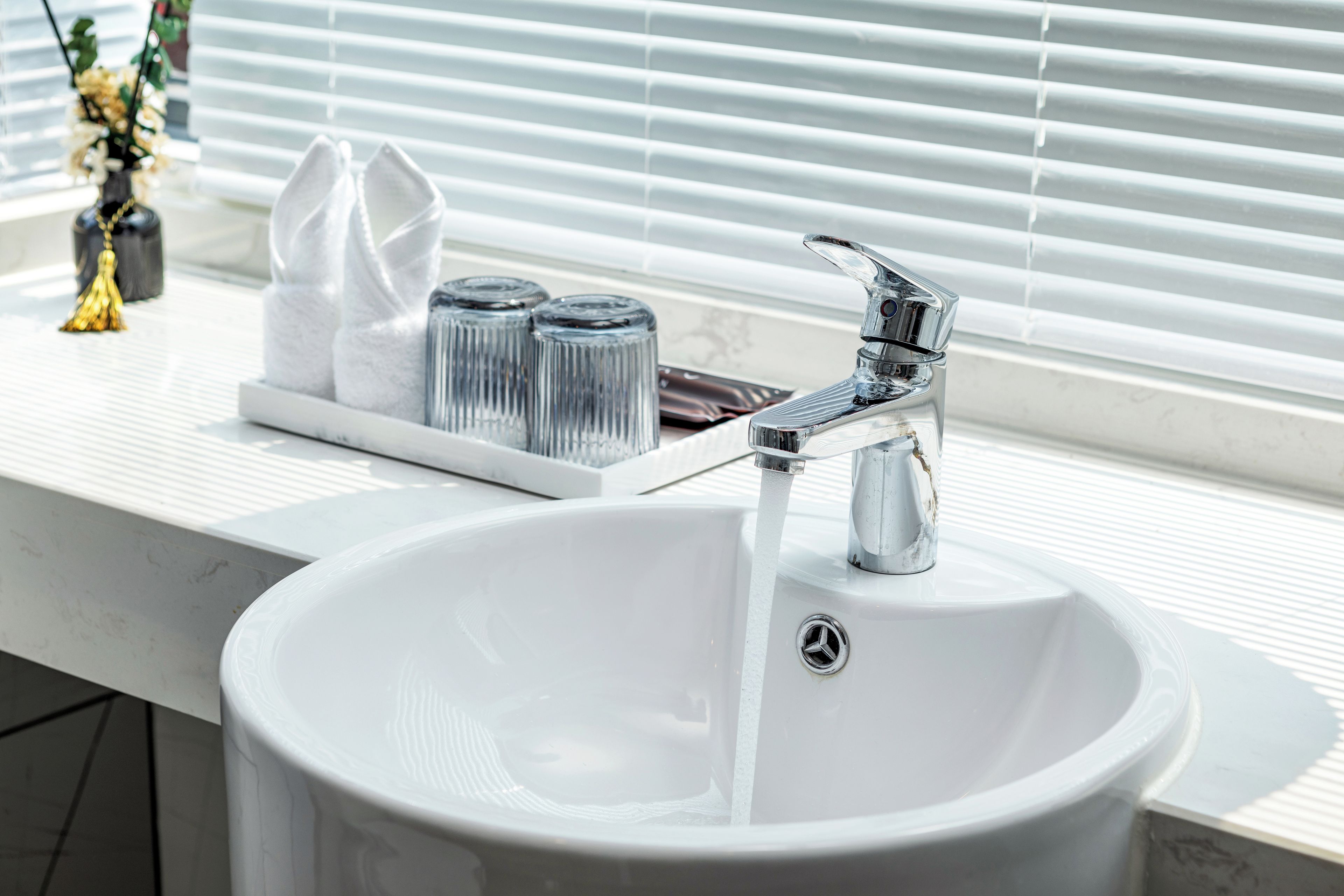 Ein weißes Waschbecken mit einem chromfarbenen Wasserhahn, einem Glas-Seifenspender und einer Seifenschale aus Glas.