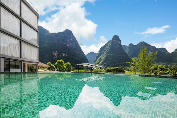 Una piscina con montañas al fondo, un edificio con amplias ventanas y cielo despejado.