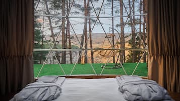 Un letto con lenzuola e asciugamani bianchi, una finestra vista su una foresta e un'altalena.