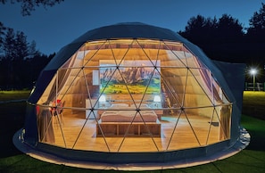 Estructura de domo geodésico con cama, mesitas de noche y vista a un paisaje montañoso.