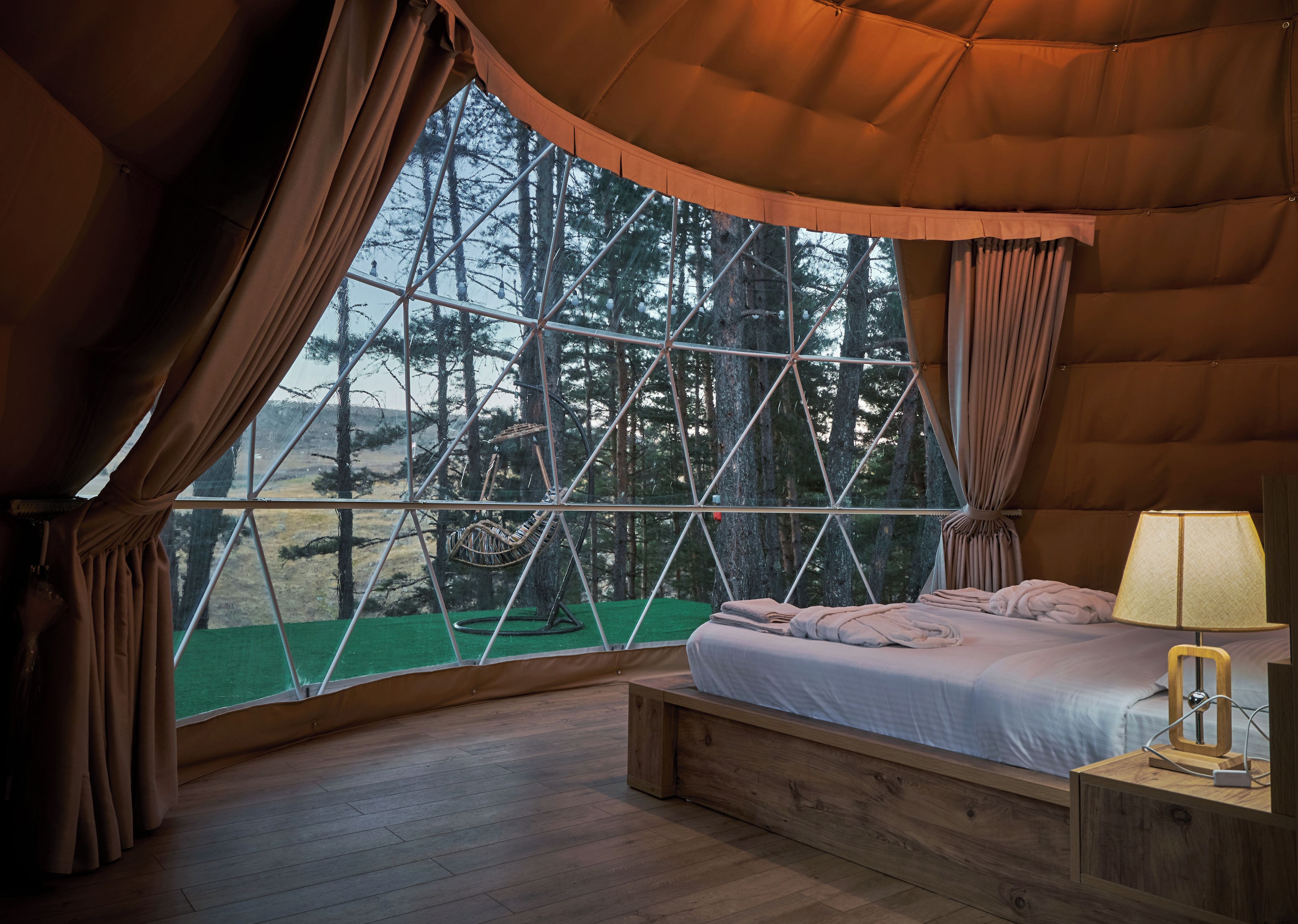 Un dormitorio acogedor con una ventana grande, una cama y una mesita de noche con lámpara.