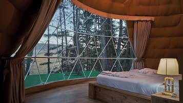 Un dormitorio acogedor con una ventana grande, una cama y una mesita de noche con lámpara.