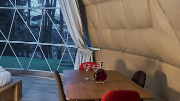 Un comedor con mesa de madera y sillas rojas, un banco y vistas a árboles a través de un ventanal grande.