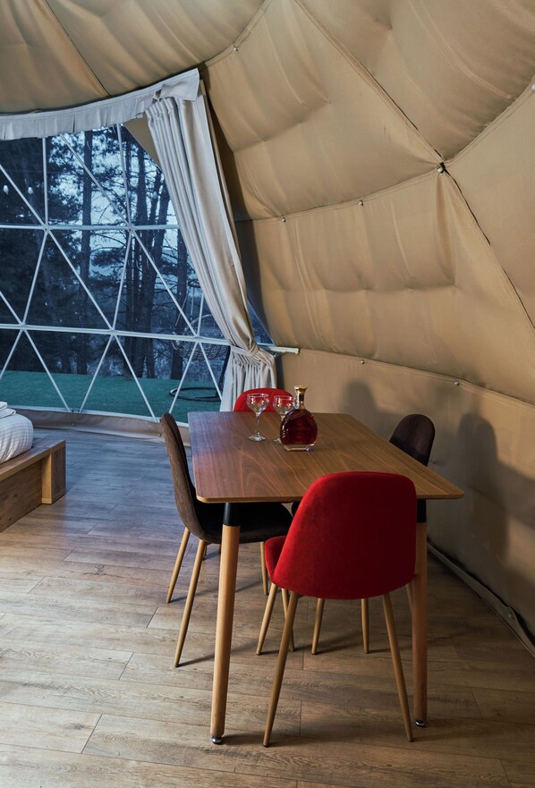 Un comedor con mesa de madera y sillas rojas, un banco y vistas a árboles a través de un ventanal grande.