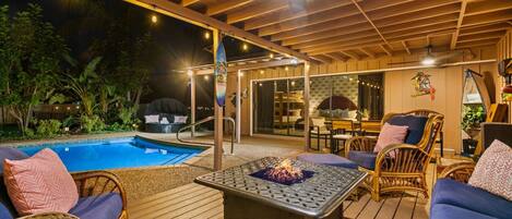 An outdoor patio with a pool, seating area, and a fire feature.