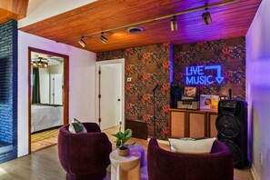 Une pièce avec un plafond en bois, un panneau néon indiquant « MUSIQUE LIVE », une grande enceinte et deux chaises violettes.