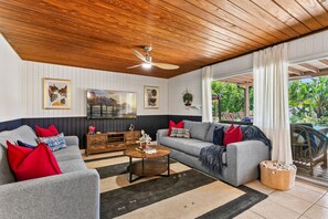 A living room with a wooden ceiling, a TV mounted on the wall, a sofa set, a coffee table, and a view of the outdoors. - Bayou Breeze| PickleBall, Pool, Sports Court | AMI (Bradenton)