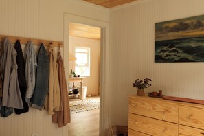 Ein Zimmer mit einem hölzernen Schminktisch, einem Meeresblicks Gemälde und einem Kleiderständer mit verschiedenen Kleidungsstücken.