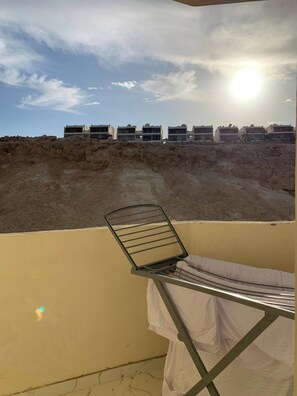 Ein Balkon mit einem Metallstuhl und einem Tisch, der auf eine Reihe von Gebäuden und eine Sandlandschaft blickt.