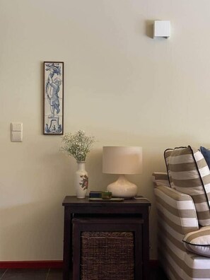 Ein Zimmer mit einer Couch, einer Lampe, einer Blumenvase und einem gerahmten Bild an der Wand.