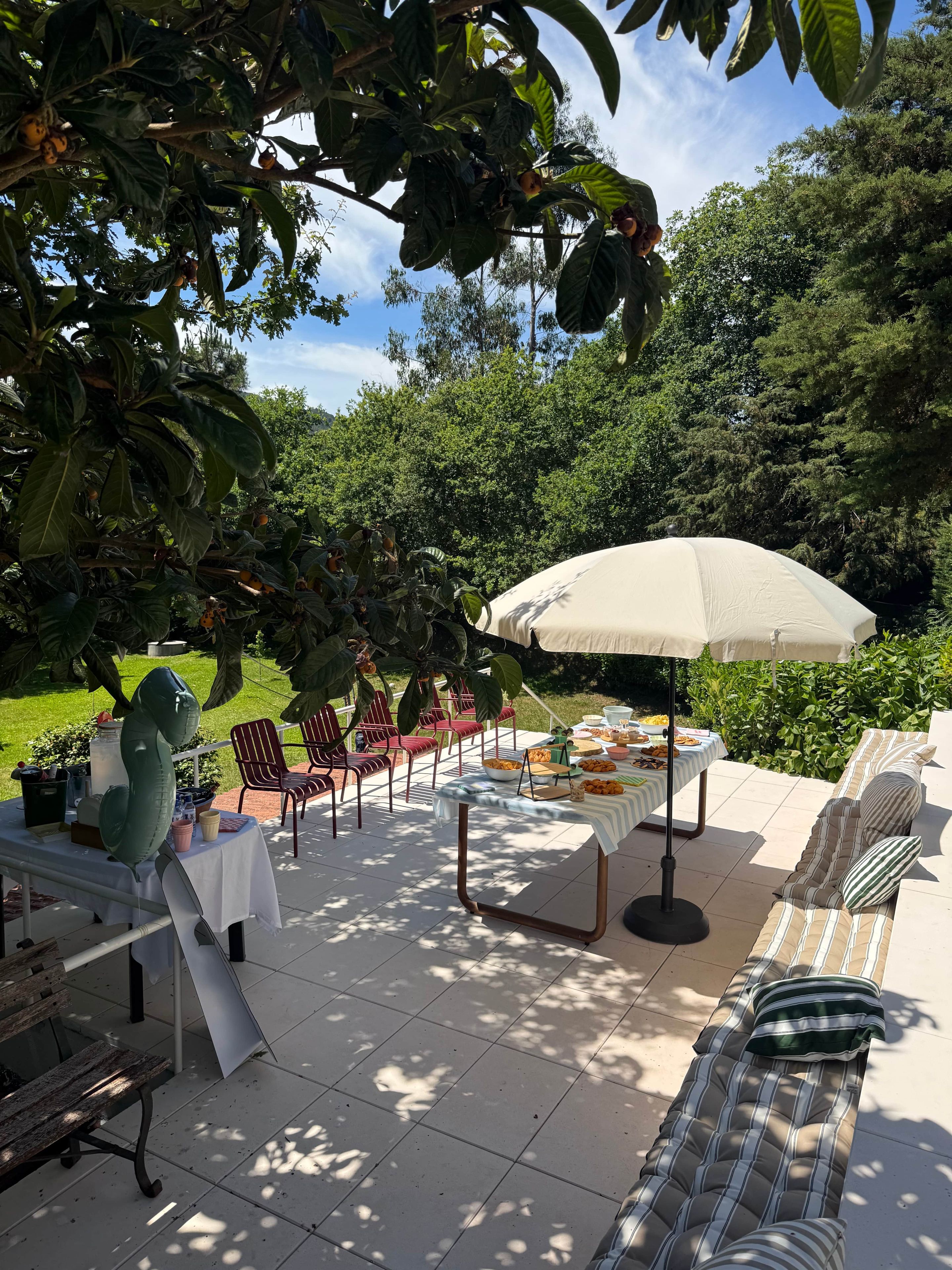 An outdoor patio with a table set for a meal, surrounded by chairs and an umbrella.