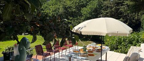 An outdoor patio with a table set for a meal, surrounded by chairs and an umbrella.