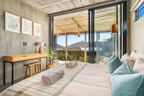 Ein Schlafzimmer mit einem großen Bett, einem Holztisch und Blick auf Berge durch große Fenster.