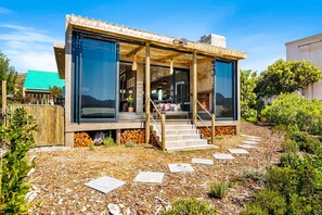 Ein modernes Haus mit überdachter Veranda, einer Treppe, die zum Eingang führt, und Blick auf die umliegende Landschaft.