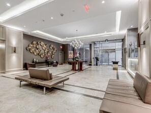 Eine großzügige Lobby mit modernem Design, ausgestattet mit einer zentralen Sitzecke mit Sofas und einem Couchtisch, einer Wand mit runden Mustern sowie einem Kronleuchter.