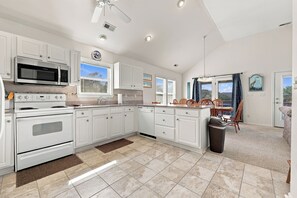 A modern kitchen with white cabinetry, stainless steel appliances, and a dining area with a view. - Walk to Beach in Duck·Hot Tub·Sound Access·Dogs OK (Kitty Hawk)