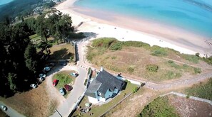 An aerial view of a coastal area with a beach, a parking lot, and a building with a sloped roof. - Villa Ofelia – A Place of Tranquility (Viveiro)